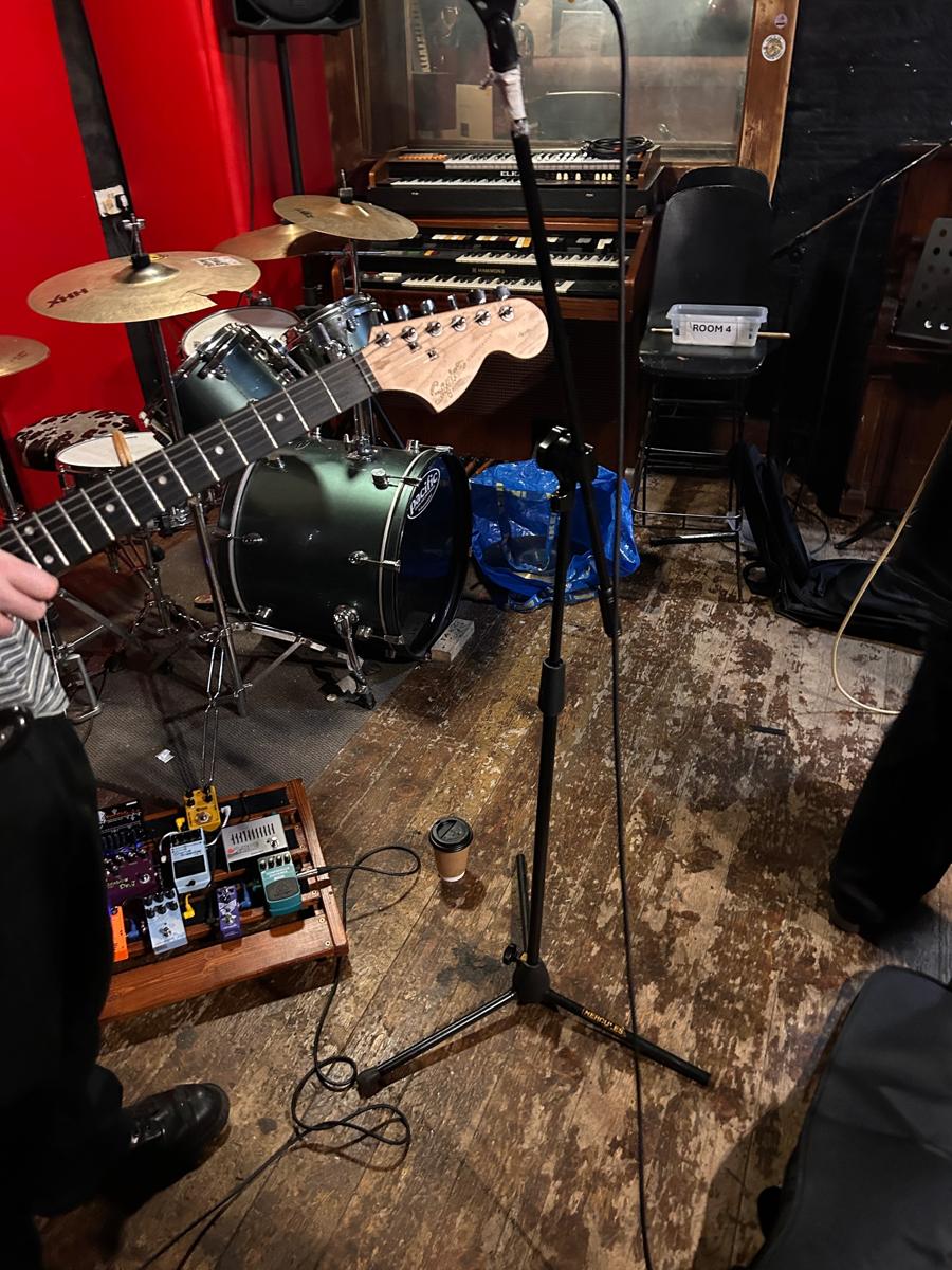 Rehearsal room with a drum kit, Hammond organ, microphone stand and a guitar neck in the foreground